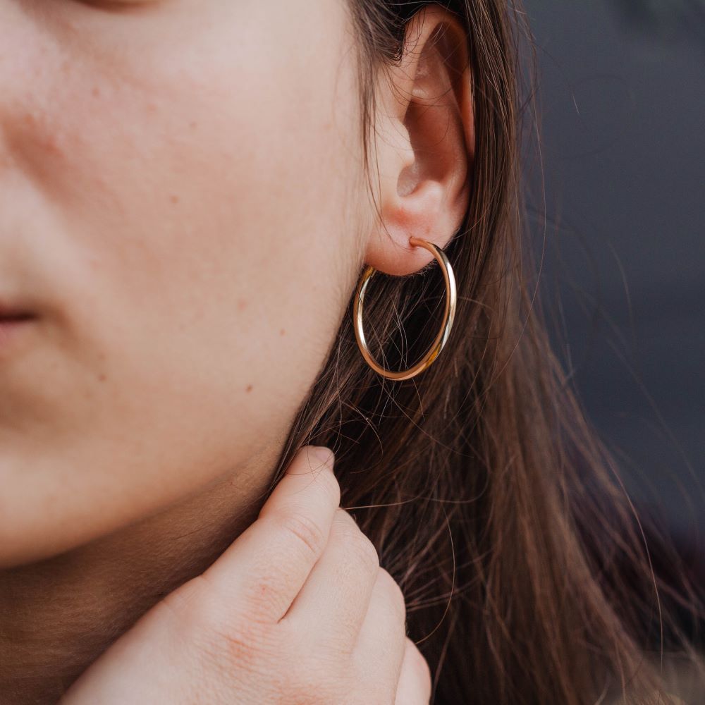 Woman wearing 14K Gold Hoop Earrings 35mm, stylish medium-sized hoops. Ideal as a gift, delivered in elegant packaging.