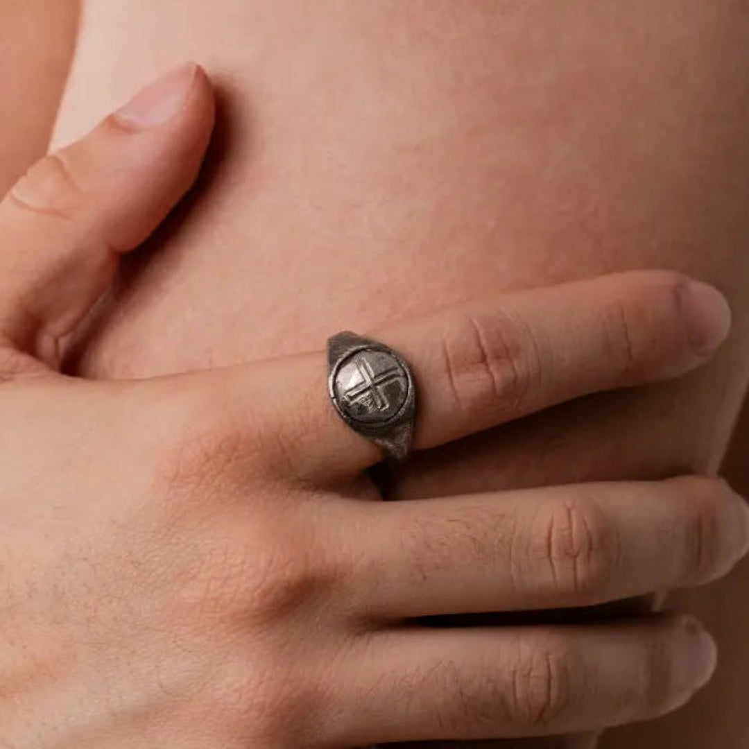 Close-up of a hand wearing a cross silver ring with a design on a neutral background