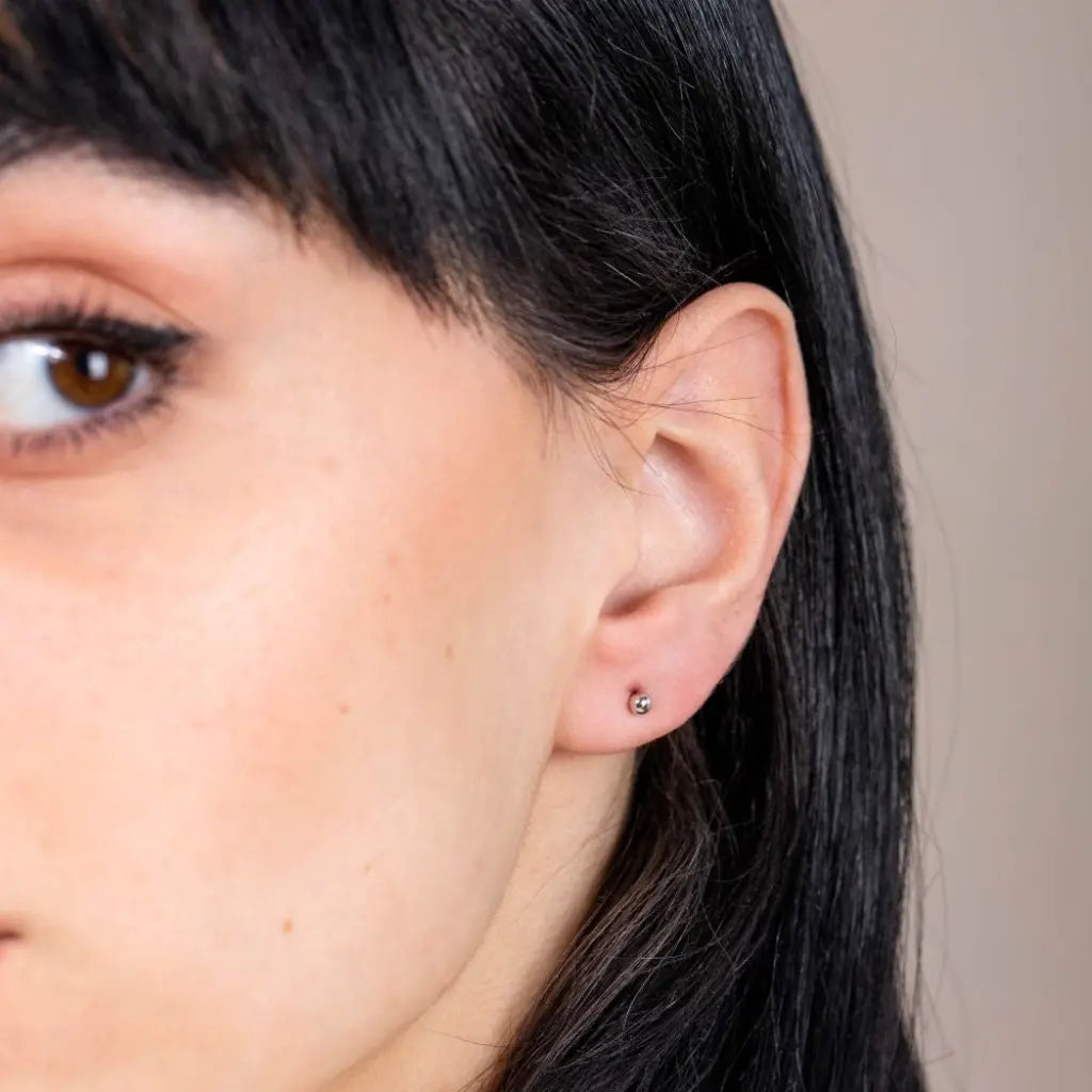 Close-up of a woman's ear wearing Tiny Ball Stud Earrings 14K Gold, showcasing minimalist 3mm solid gold design.