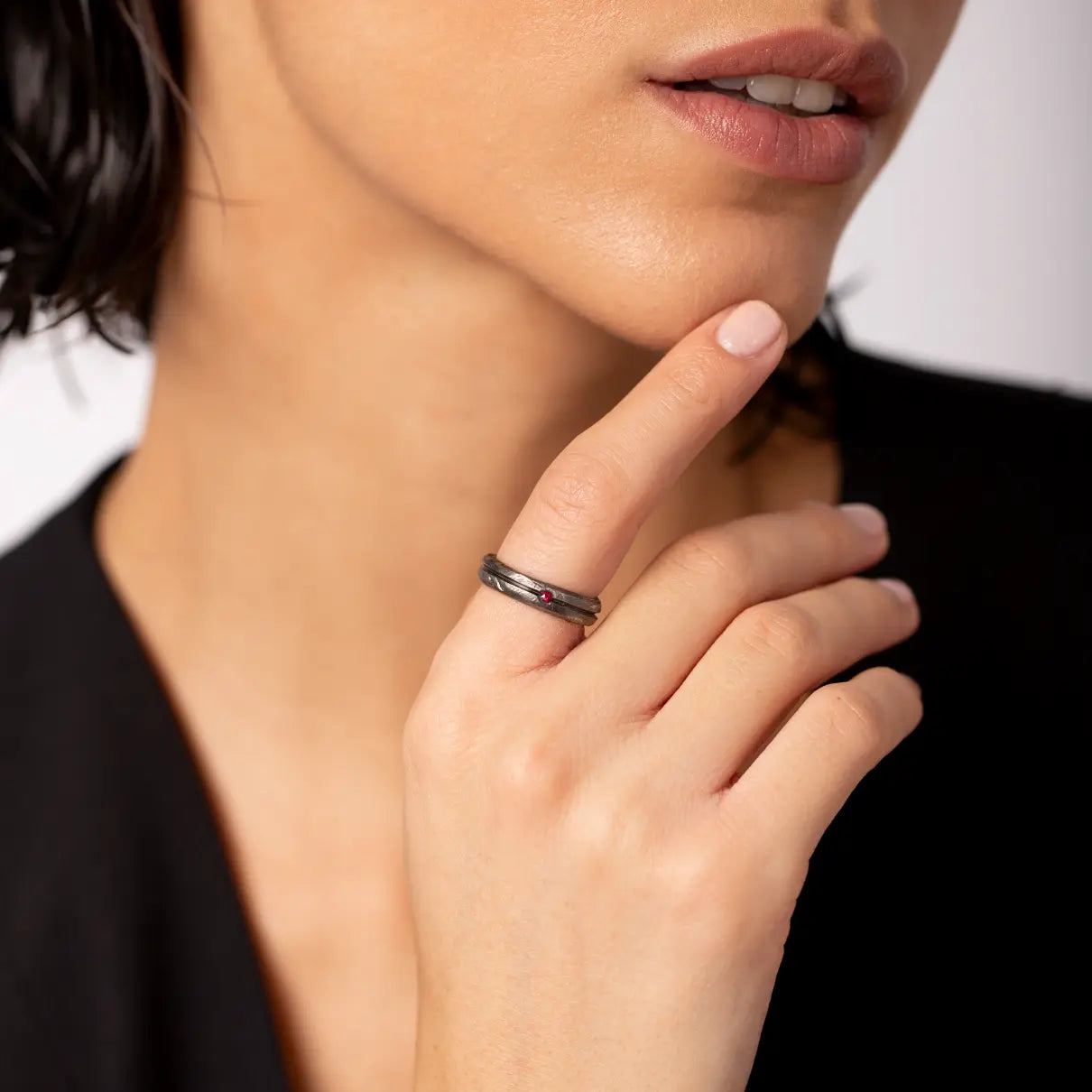 Close-up of a hand wearing the Ruby Narrow Band Ring Oxidized Silver 925, featuring a black oxidized sterling silver finish and a small natural ruby.