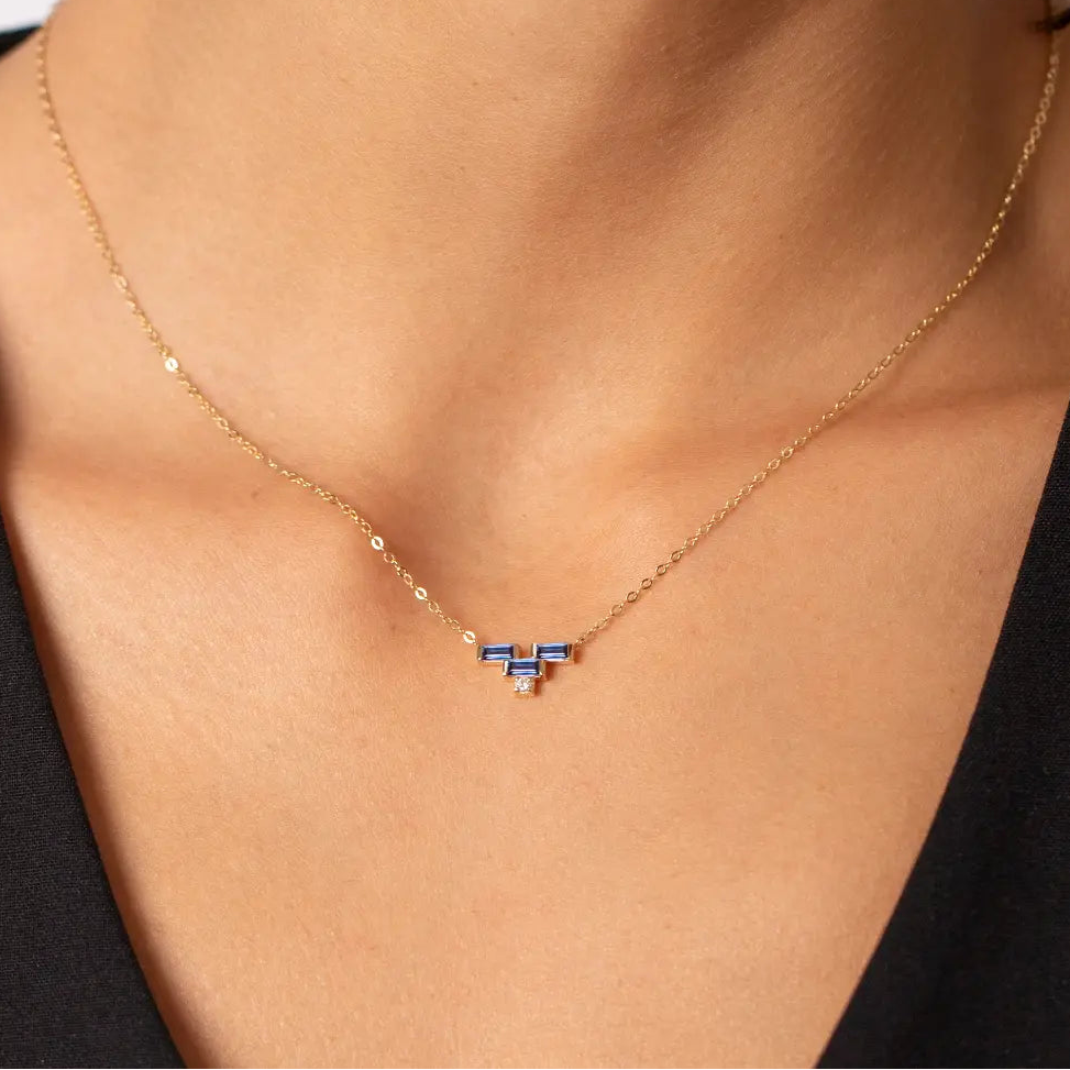 Gold necklace with a blue sapphire on a woman wearing a black top.