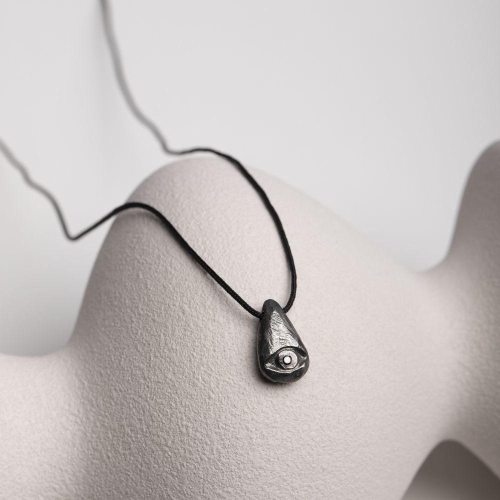 Oxidized silver evil eye necklace with black diamond on sculptural background.
