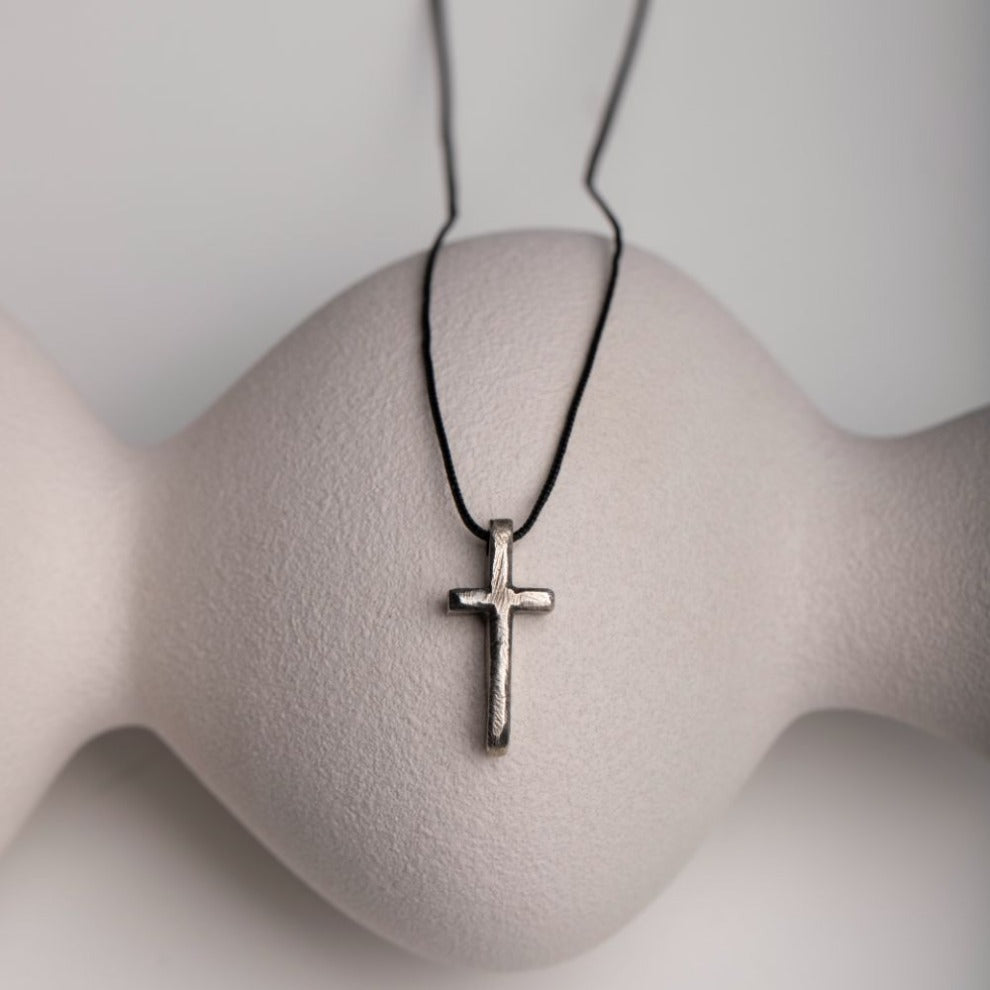 Men's sterling silver cross necklace with black oxidized finish displayed on a modern stand.