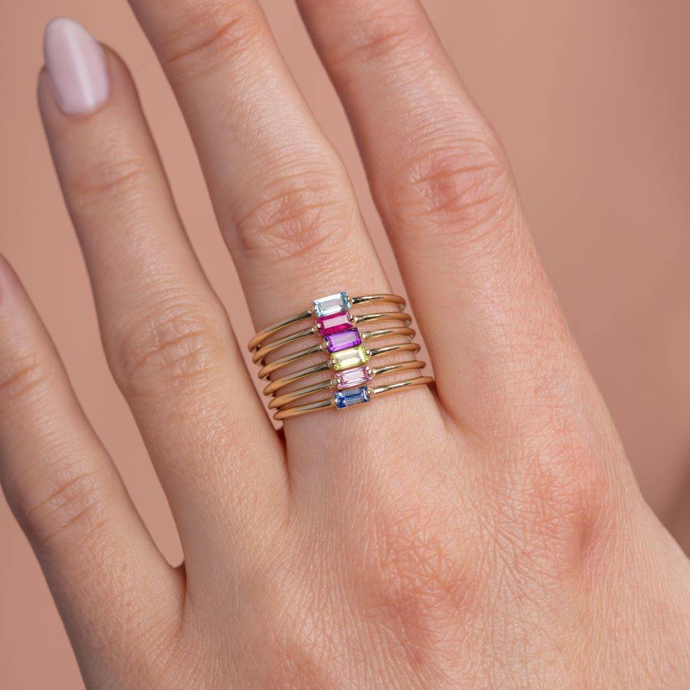 Gold band with purple amethyst baguette ring stacked on woman's finger, showcasing minimalist jewelry.
