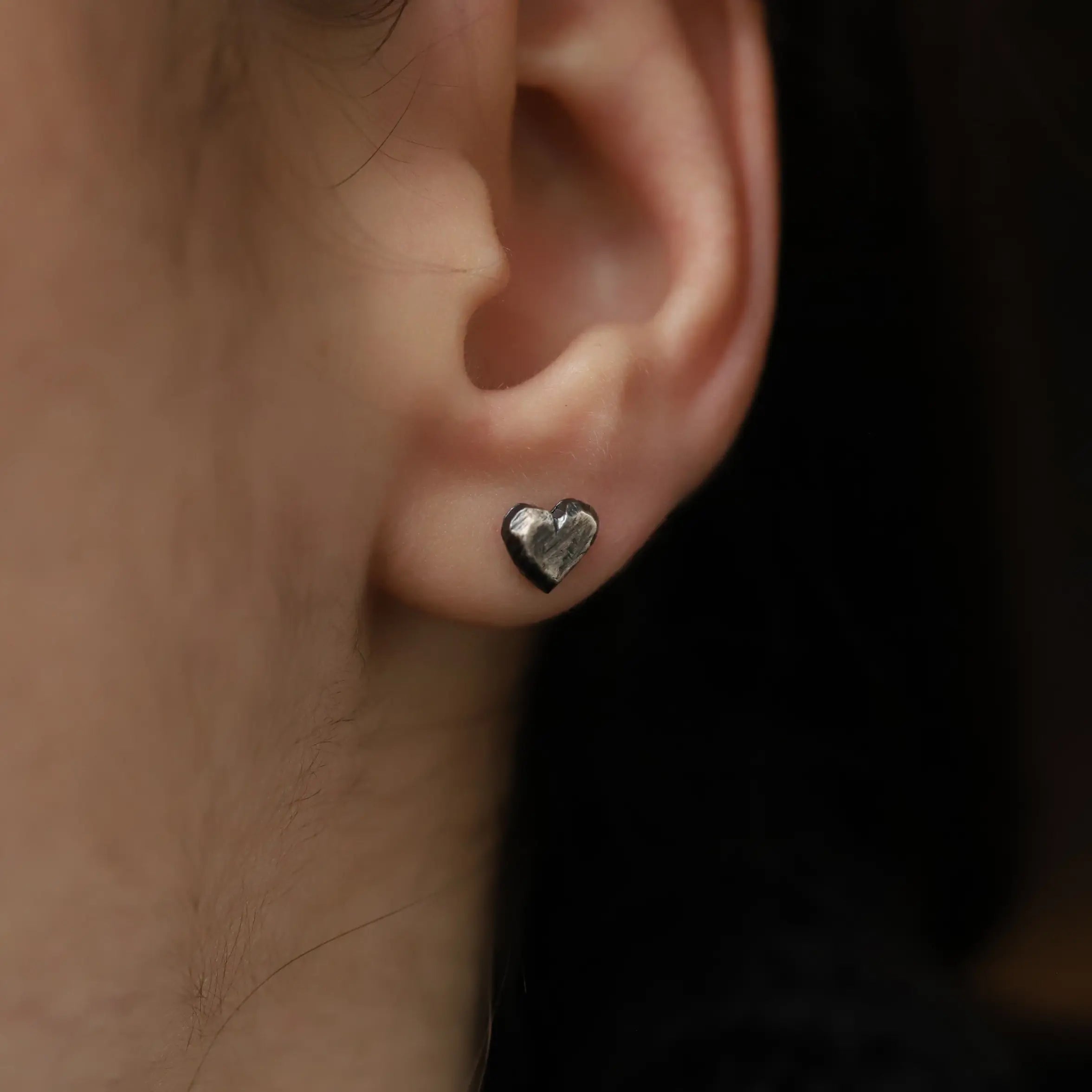 Close-up of Oxidized Silver Heart Stud Earrings on an ear, handmade from sterling silver 925, suitable for men and women, 6mm x 7mm size.