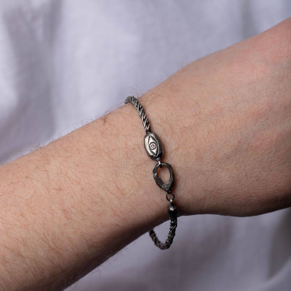 Person wearing oxidized silver evil eye bracelet featuring black diamond, suitable for unisex streetwear fashion jewelry.