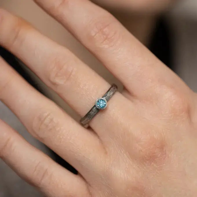 Hand wearing a London Blue Topaz ring on oxidized 925 sterling silver band, showcasing a unique brutalist design.