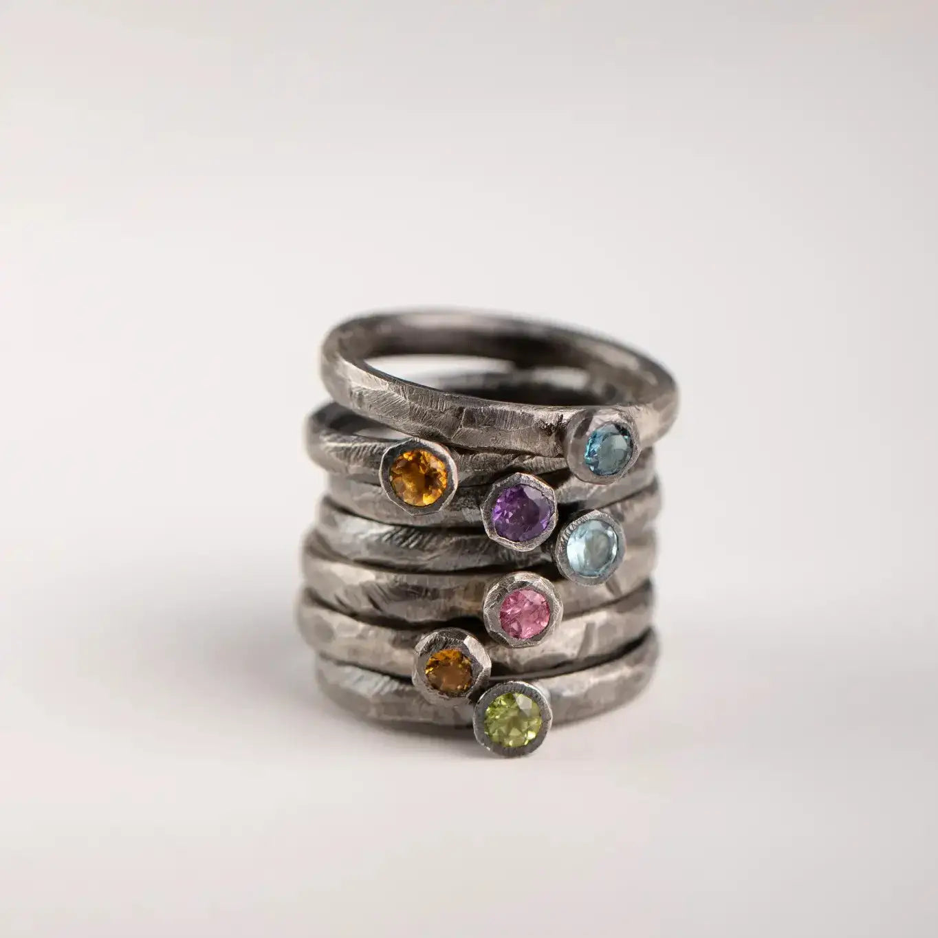 Stack of 925 oxidized silver rings with colorful gemstones, including topaz, set against a neutral background.