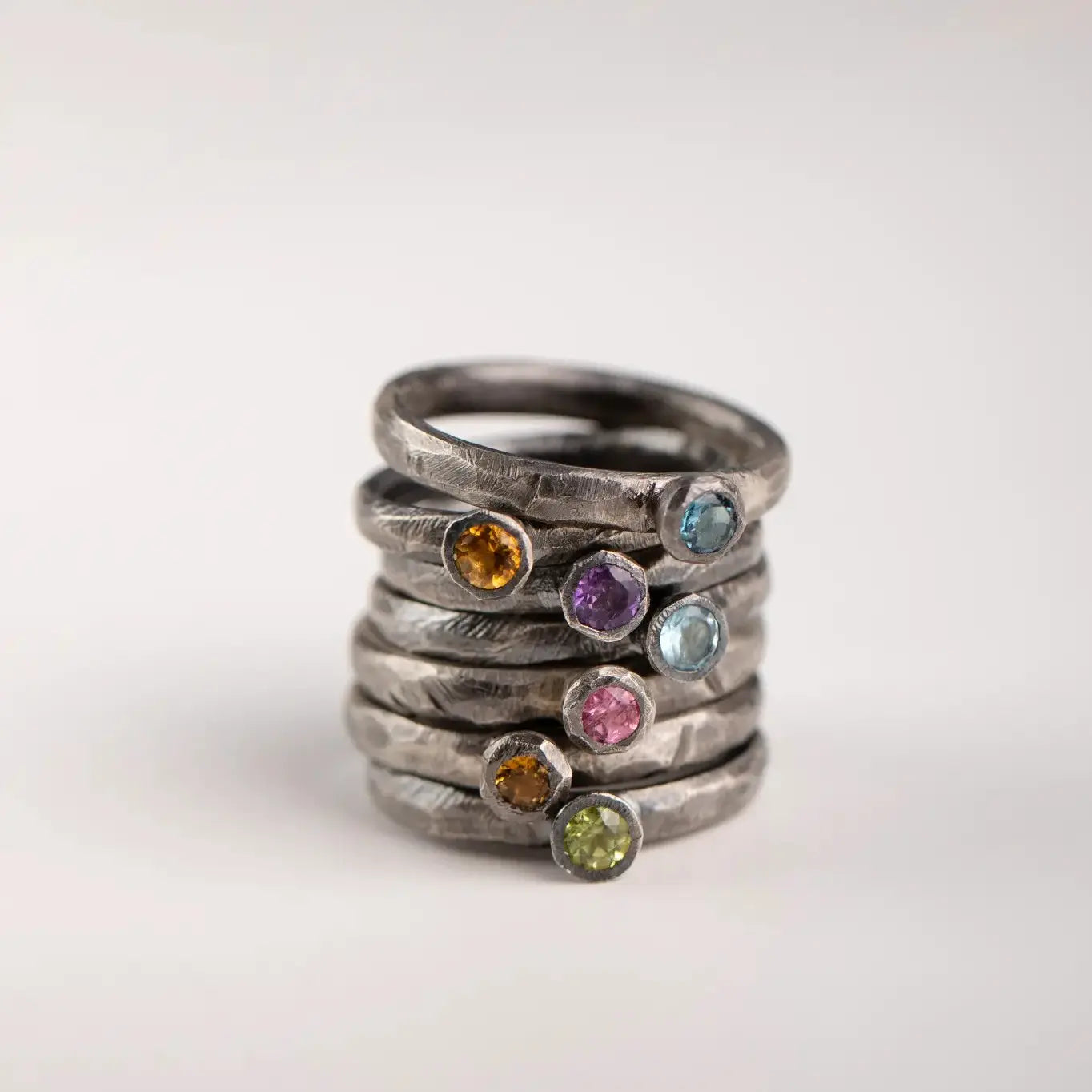 Stack of oxidized silver rings with colorful gemstones, including citrine, showcasing artisan craftsmanship and unique design.