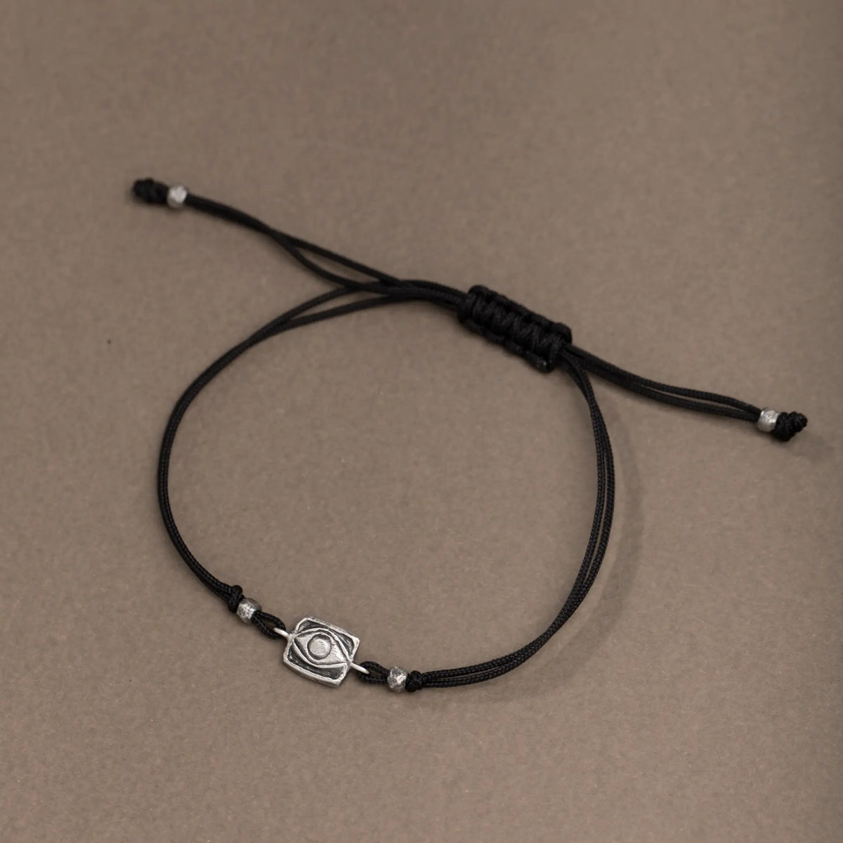 Adjustable small evil eye bracelet with black cord on gray background