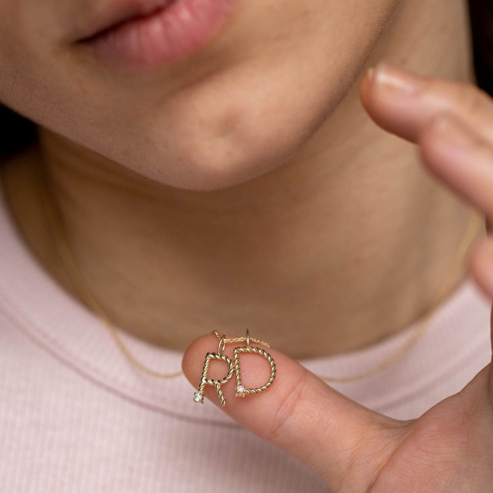 Diamond Initial Necklace 14K Gold held by person, twisted monogram with diamonds, brilliant cut, 16-inch chain, elegant handcrafted jewelry.