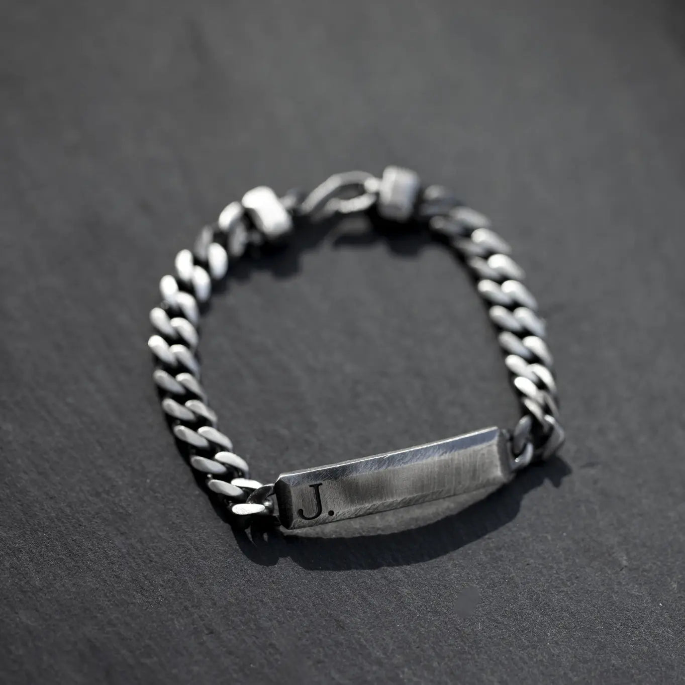 Personalized sterling silver ID bracelet with dark oxidized bar and curb chain, perfect handcrafted gift for him, on dark surface.