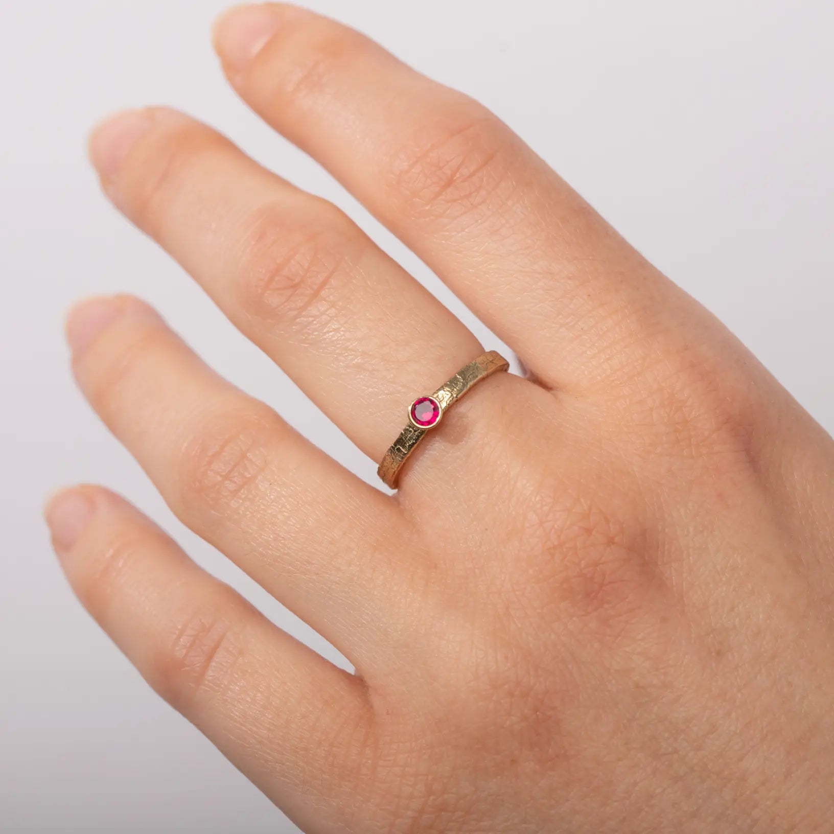 Dainty textured Birthstone Ring Sterling Silver with pink stone on finger, elegant design, 925 silver, gold finish, personalized jewelry.