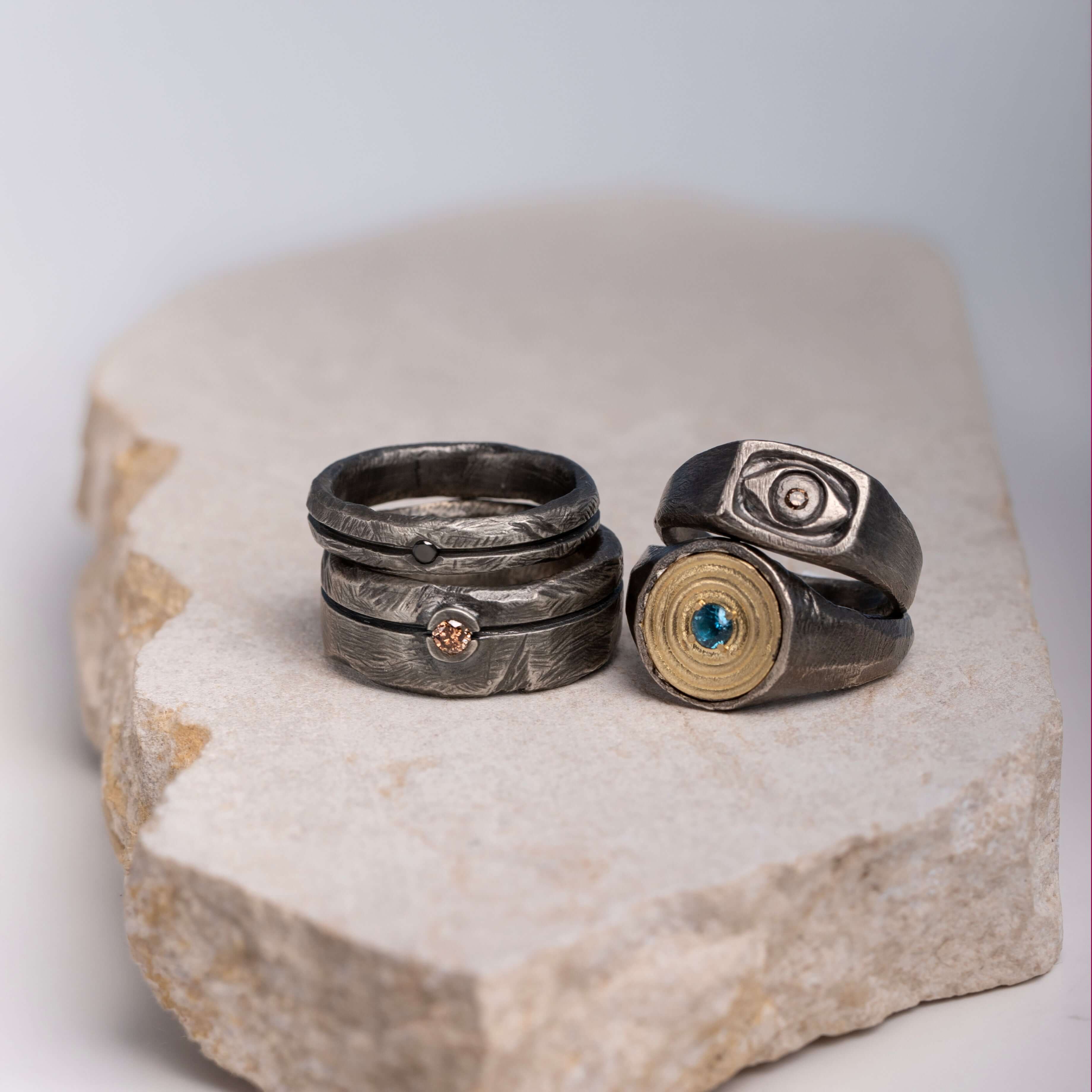 Rings featuring different gemstones on a stone surface, representing The Meaning Behind the Gemstones in Kyklos Jewelry.