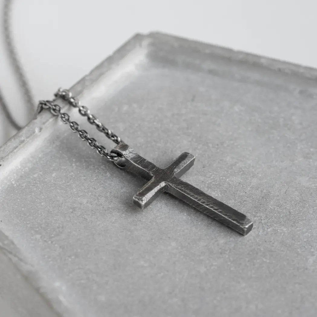 Cross Necklace Men Oxidized Silver resting on a gray surface, showcasing its bold design and premium silver craftsmanship.