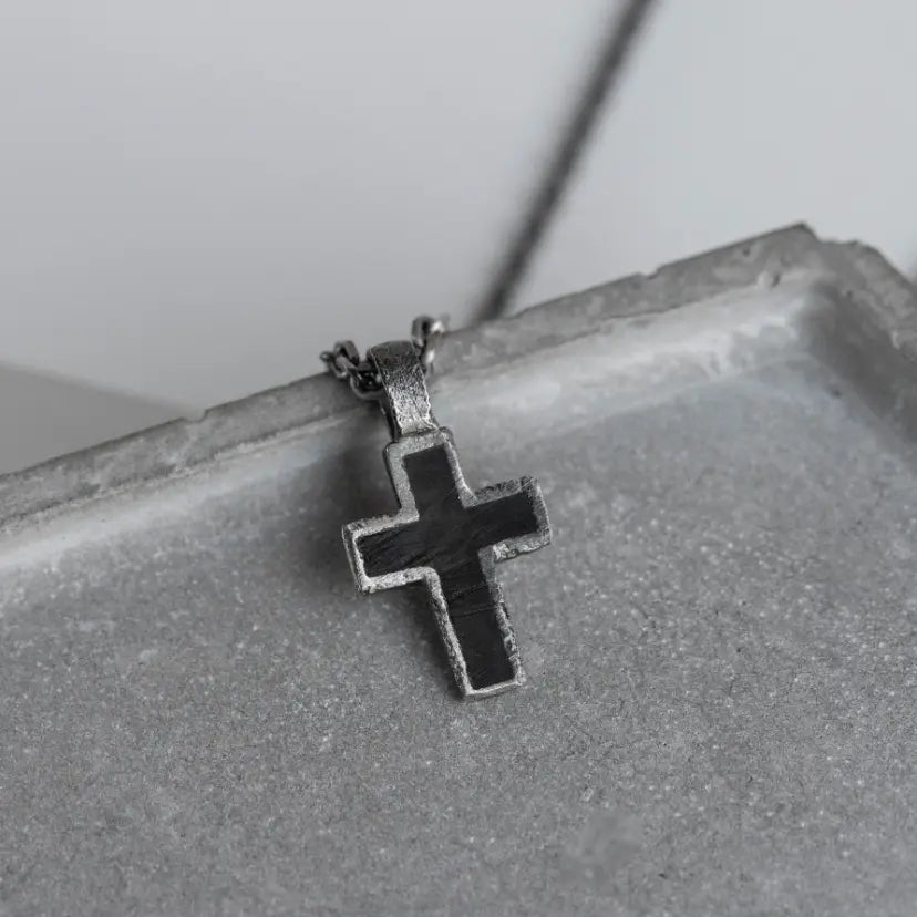 Close-up of a Silver Cross Necklace Black Enamel displayed on a concrete surface, featuring sleek design and modern aesthetic.