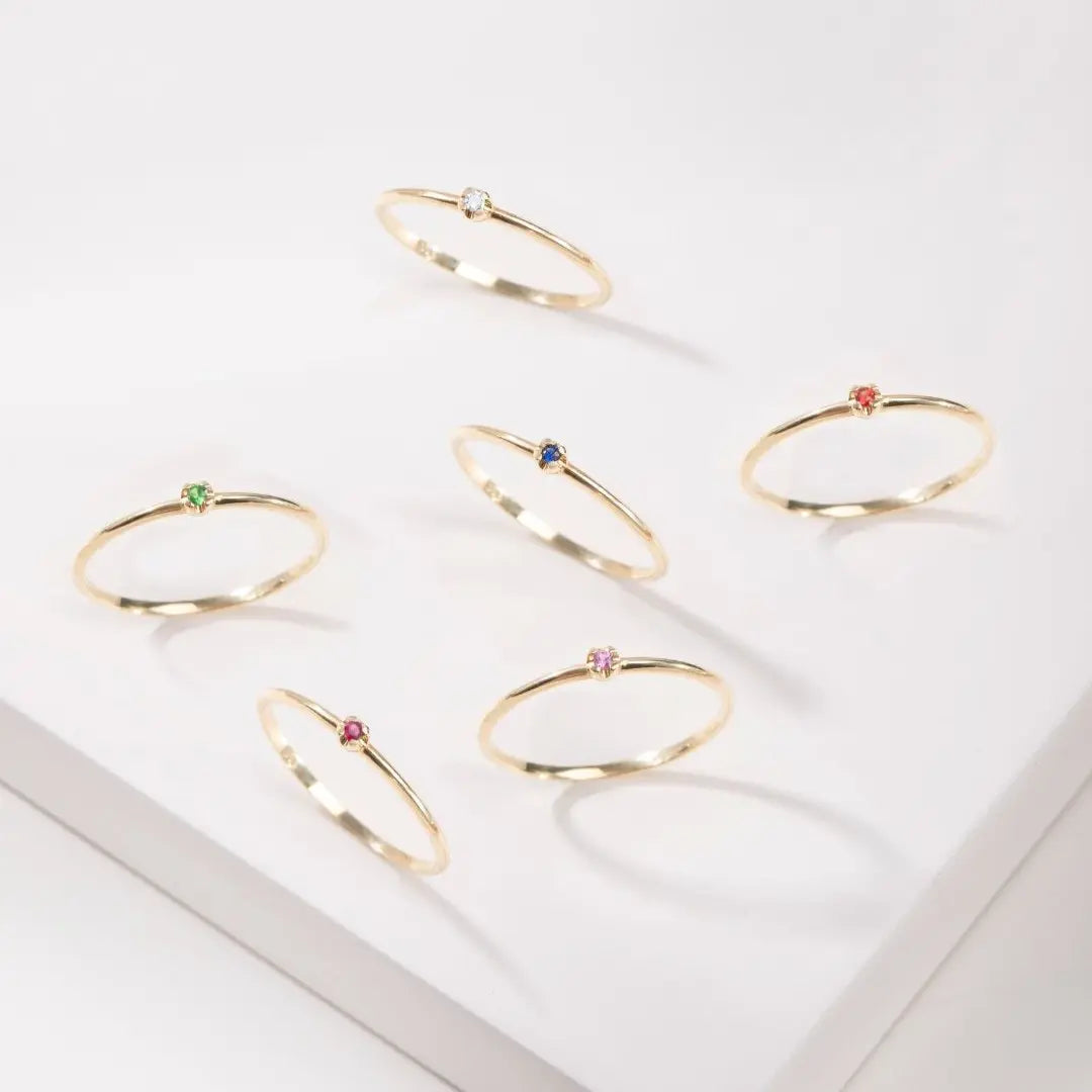 Set of gold rings with sapphire, emerald, and diamond on a white surface
